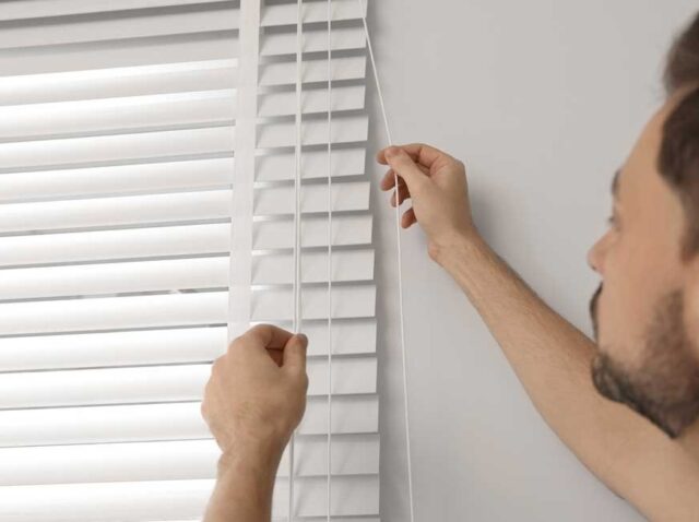 Manual outdoor blinds being adjusted by homeowner for light and privacy control in a modern home interior